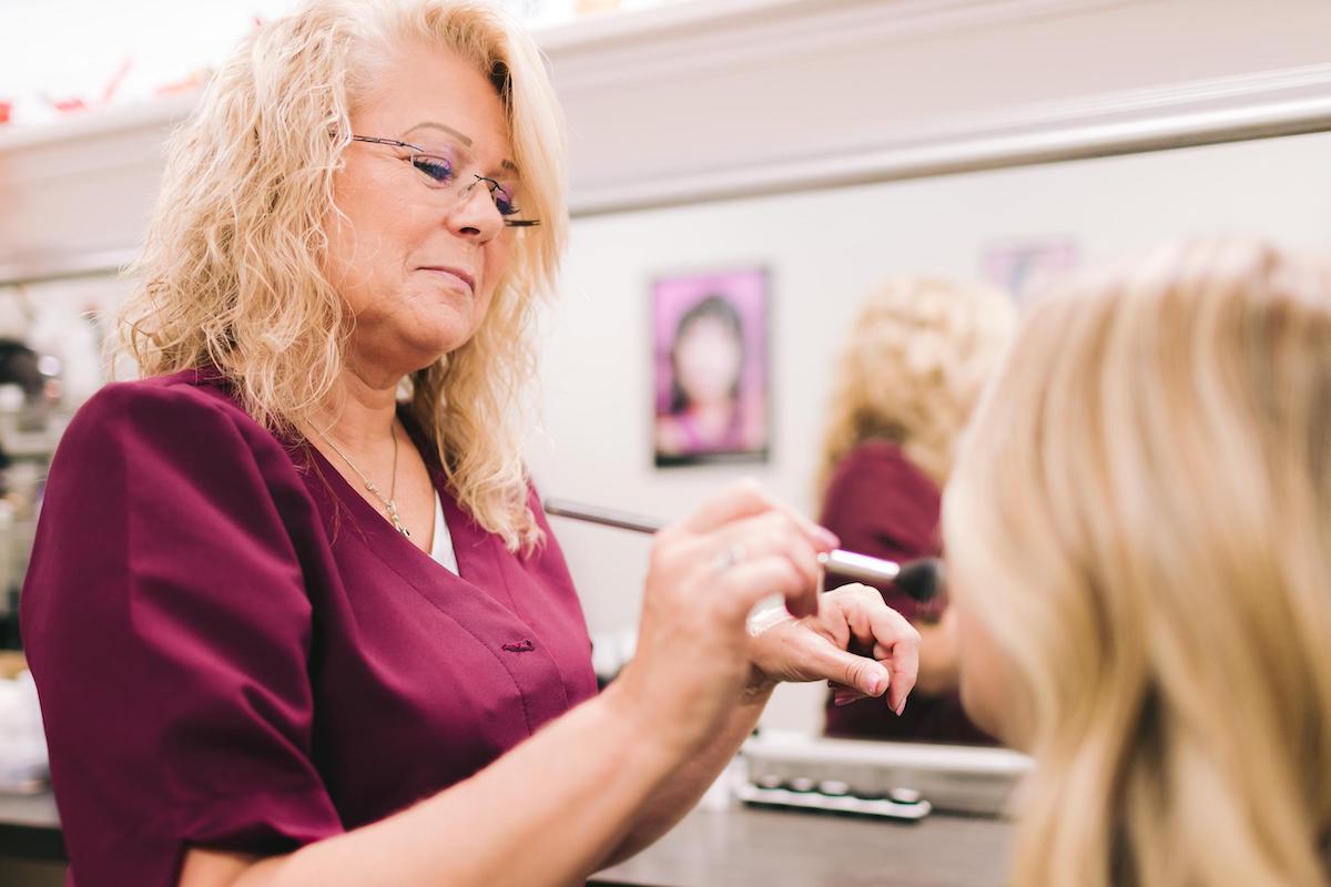 a female entrepreneur applying a makeup on her client, showcasing her personal branding and beauty expertise.